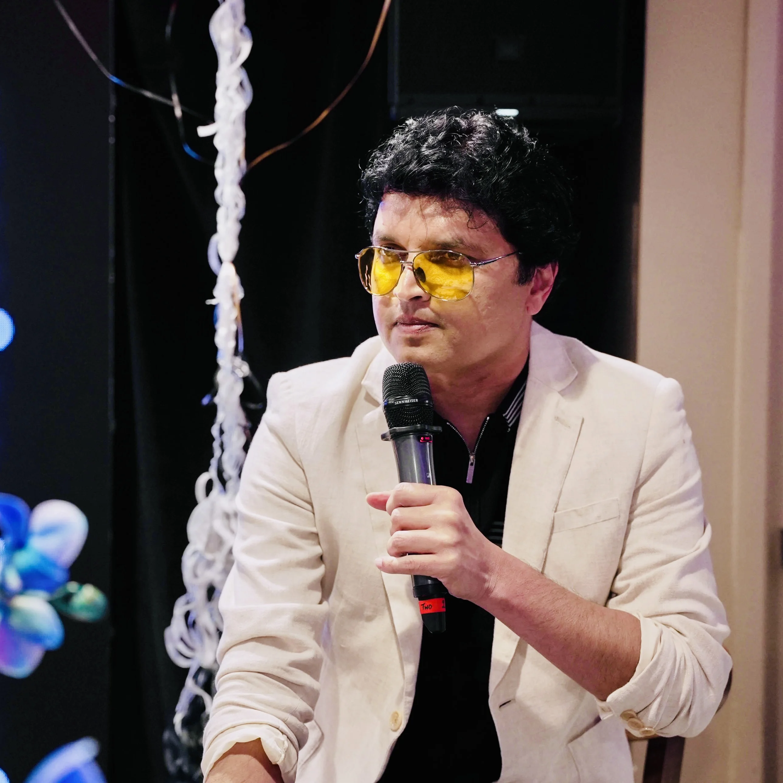 Vishal seated with a microphone, wearing yellow glasses and a cream jacket